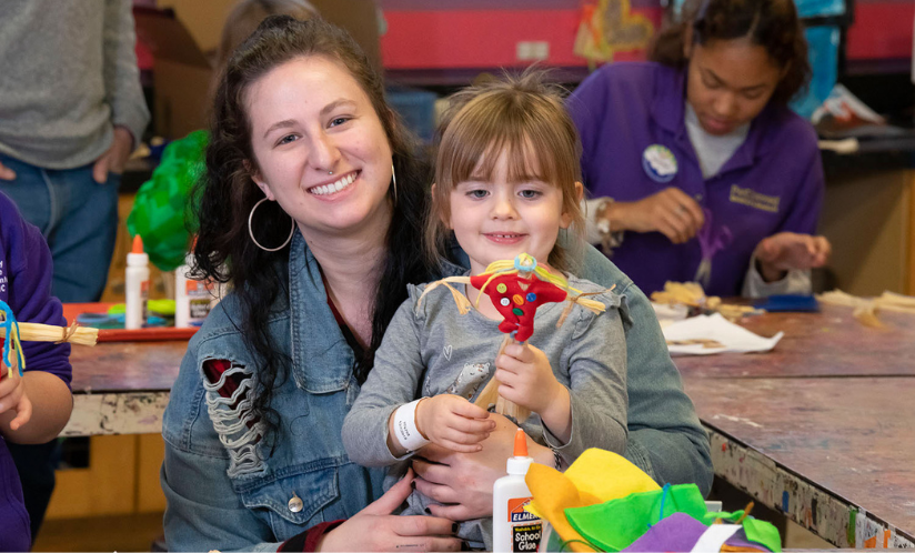 An adult and a child smiling as they look at an art project they have created at Port Discovery