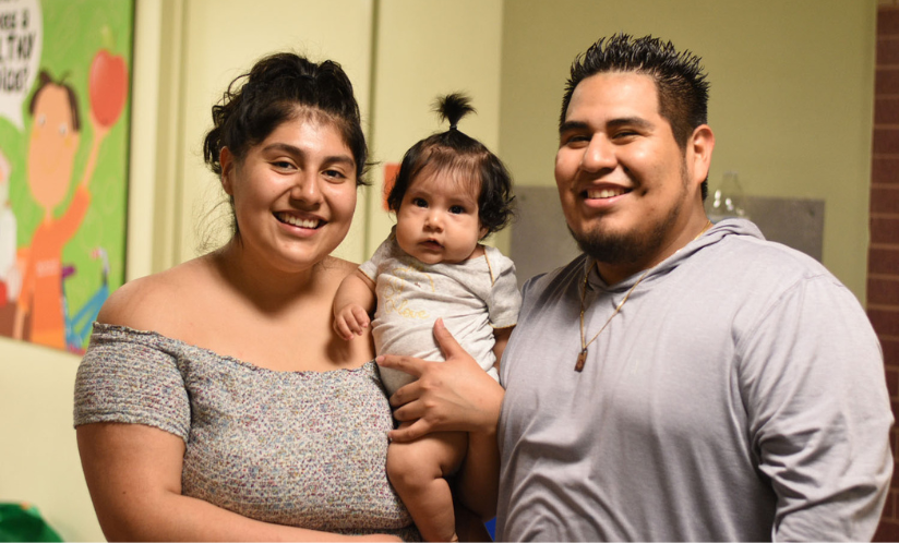 Two adults smiling and holding an infant while visiting and enjoying family time at Port Discovery Children's Museum