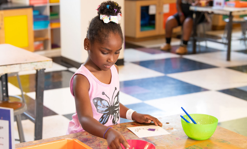 A girl standing at a table in an art studio as they work on a small art and drawing project