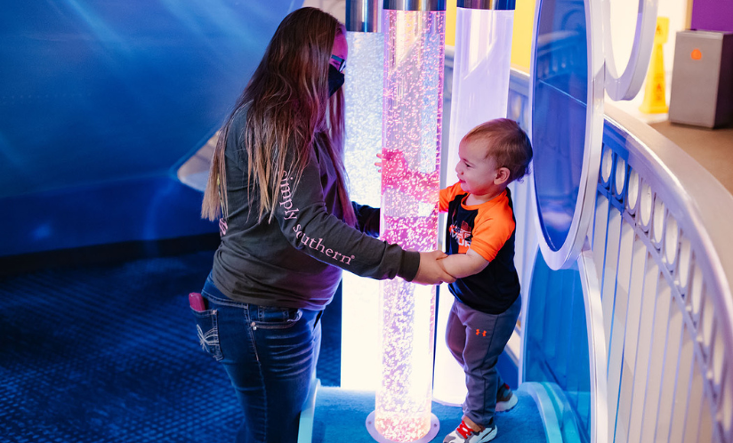 Adult and child playing on and touching lighted bubble tubes featured in one of Port Discovery's interactive play areas for toddlers