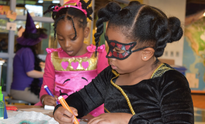 Two children wearing costumes work on an art project while attending a fall Halloween event at Port Discovery
