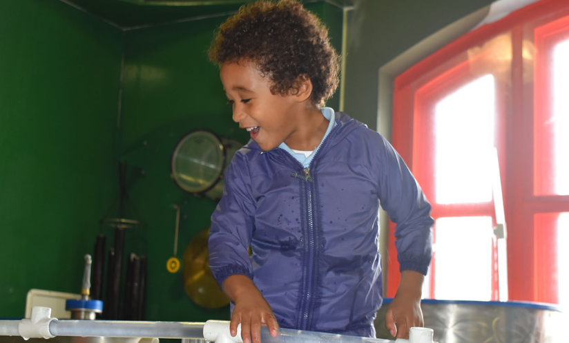 A child smiles with astonishment while playing in a water activity at Port Discovery