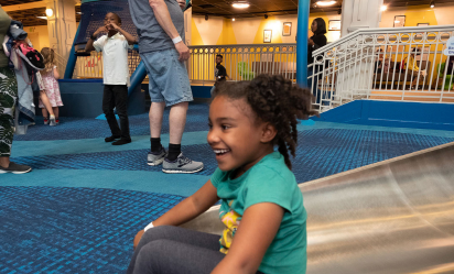 A side view of a smiling child landing at the bottom of Port Discovery's giant slide