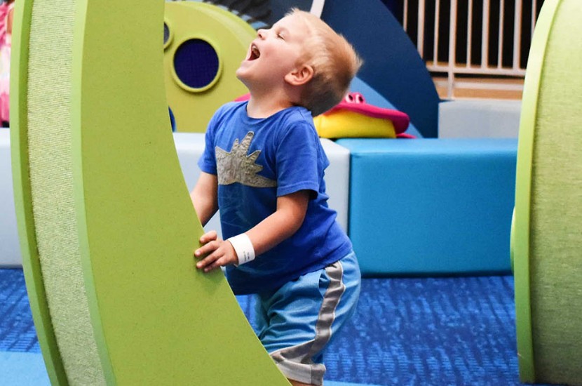 A child looking up in excitement as they touch and climb up a green structure that resembles a friendly sea creature