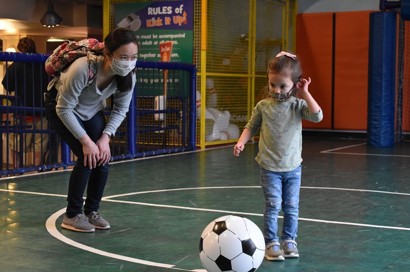 An adult and a child playing and getting ready to kick a soccer ball in one of Port Discovery's indoor play areas