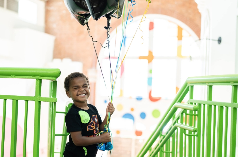 A child smiling and holding a giant bunch of blue, green and black balloons