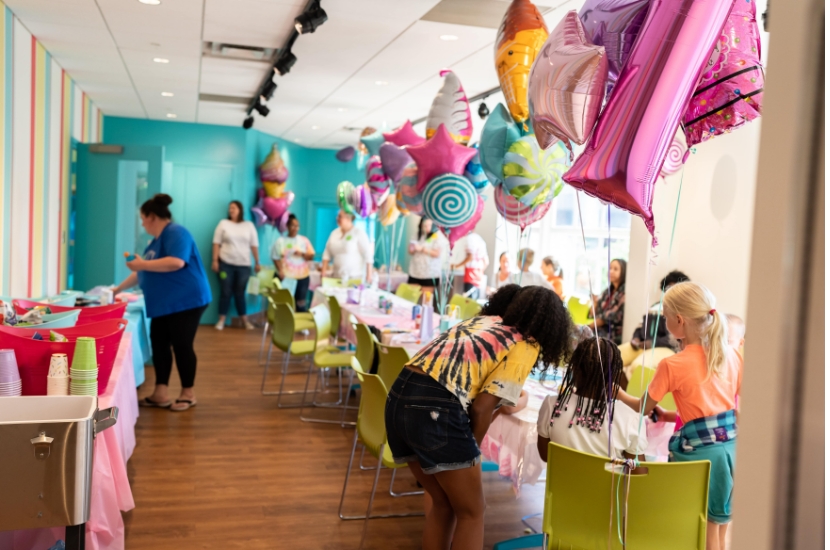 A group of adults and children gather in a colorful, private party room at Port Discovery for a child's birthday celebration
