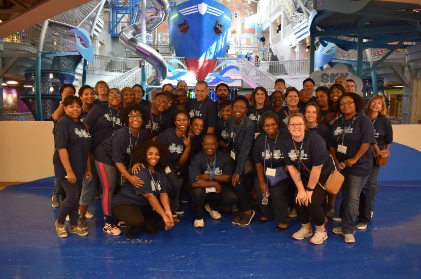 A group of adults pose under Port Discovery's giant Ship and SkyClimber exhibits for a group photo