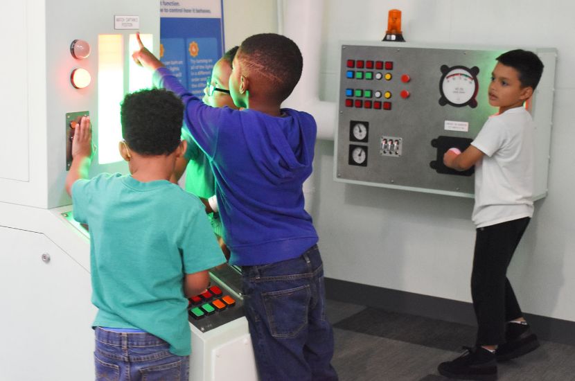 A group of children pointing at lights and playing with various levers and buttons in Port Discovery's Engine Room