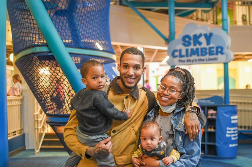 Two adults smiling and holding two children after playing and having fun together at Port Discovery