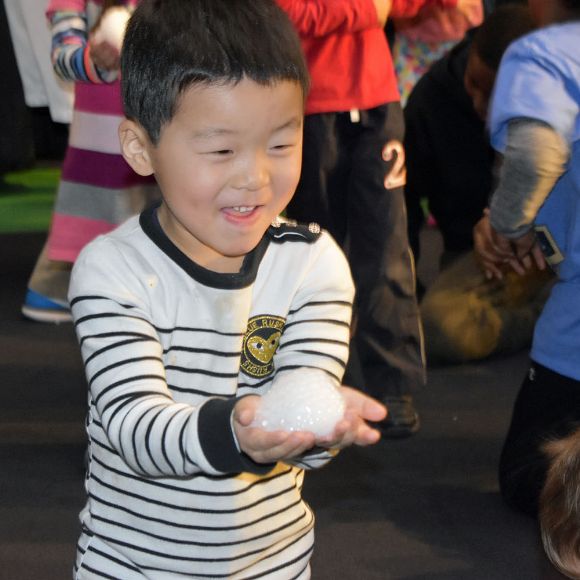 A child smiles and laughs while holding a handful of bubbles during a fun science activity at Port Discovery