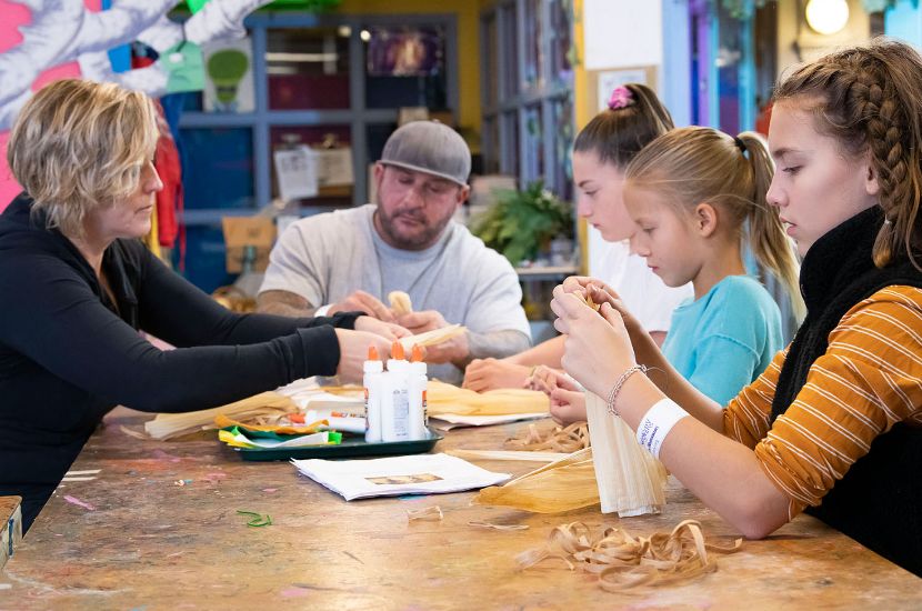 Two adults and three children sit around a table in Port Discovery's studio workshop as they work on an art project