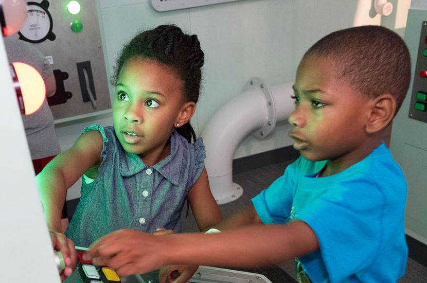 Two children playing with levers and lights featured in Port Discovery's interactive pretend engine room
