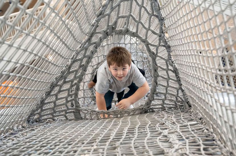 A child smiles and climbs as they work their way up a netted structure that spans at least three floors