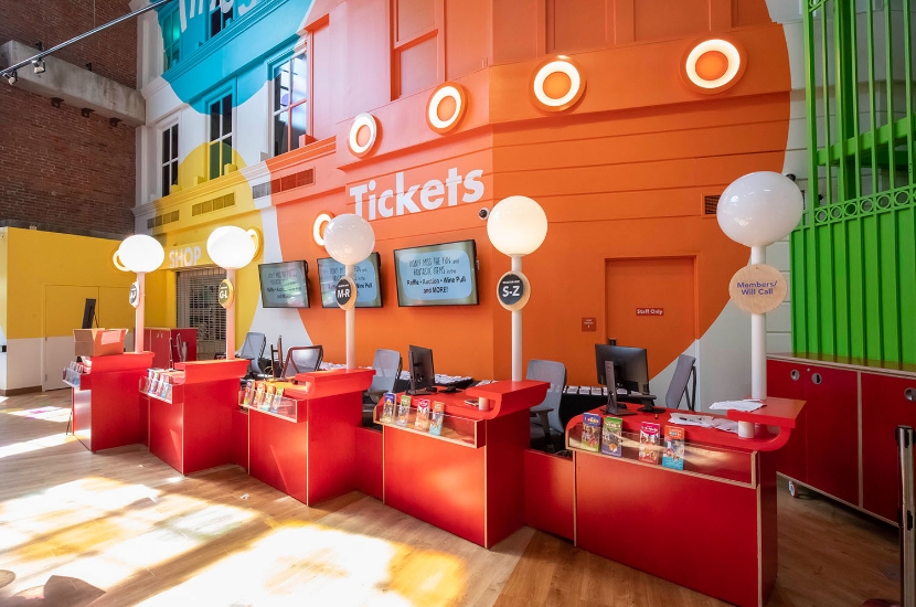 A group of red checkin stations in a colorful lobby entrance set up to welcome guests as they attend a private event at Port Discovery