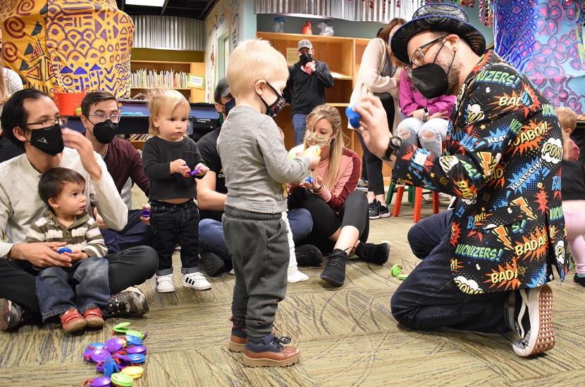 A young child interacting with a Port Discovery staff member while a group of children and adults look on