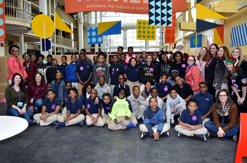 A large school group featuring children and adults pose for a photo after participating in a field trip at Port Discovery Children's Museum