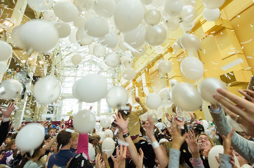 A bunch of white balloons falls from the ceiling towards the outstretched hands of people at a Port Discovery event