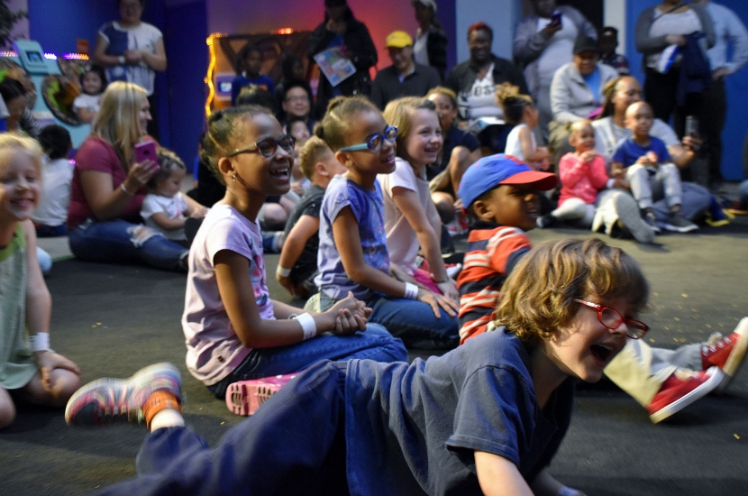 A group of children laughing and smiling while watching an interactive performance at Port Discovery Children's Museum