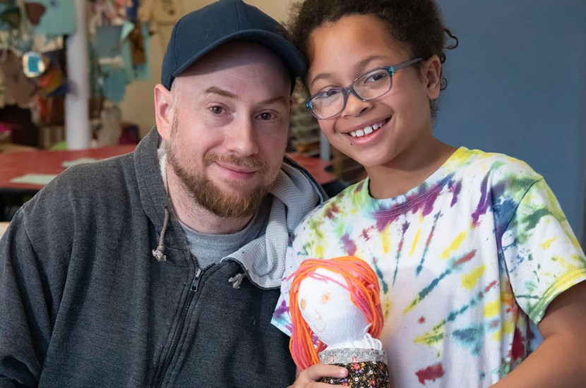 A man and a child smiling as they hold up sock puppets they created together in Port Discovery's art studio