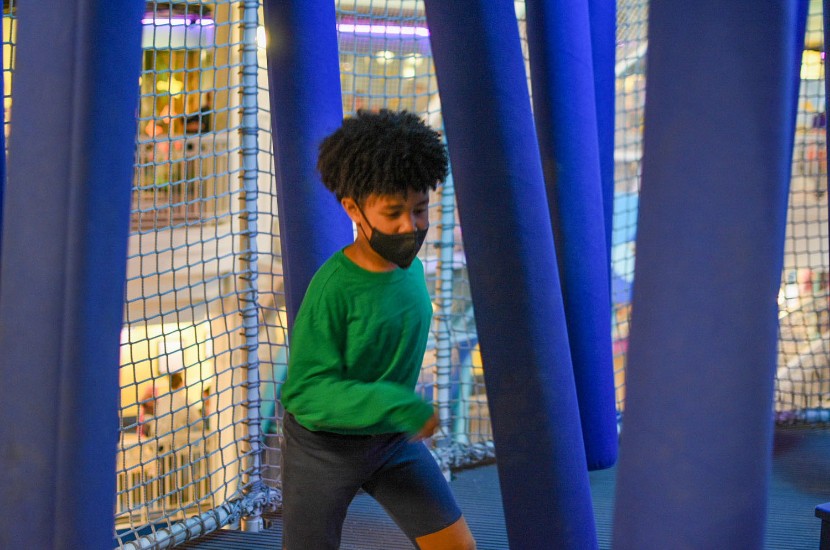 A boy running through soft, moving blue bars in a netted play area