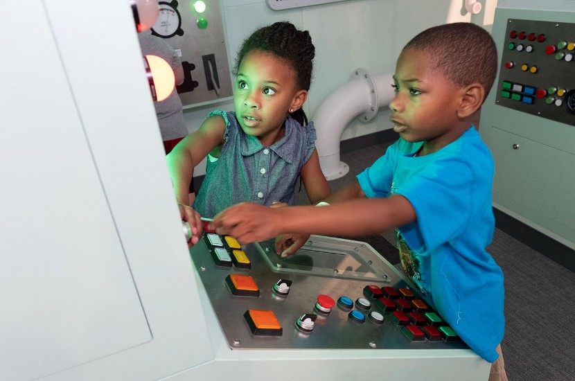 Two children playing with levers and lights featured in Port Discovery's interactive pretend engine room