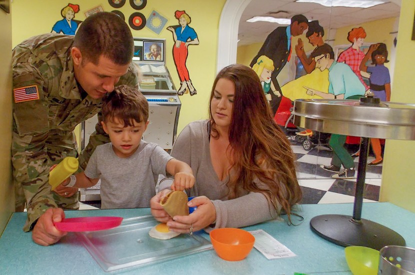 Two adults and a child playing together with pretend food and cookware at a table in Port Discovery's play diner