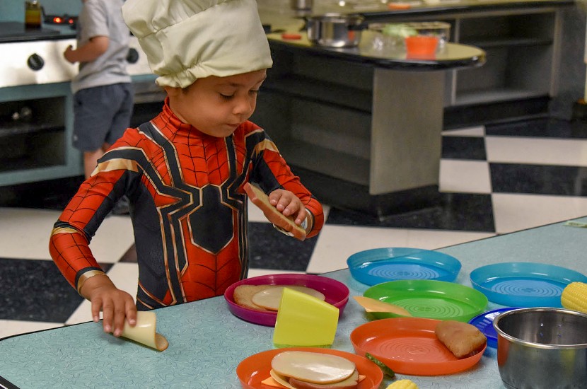 A child wearing a chef's hat and spiderman costume playing with pretend food and cookware in Port Discovery's play diner