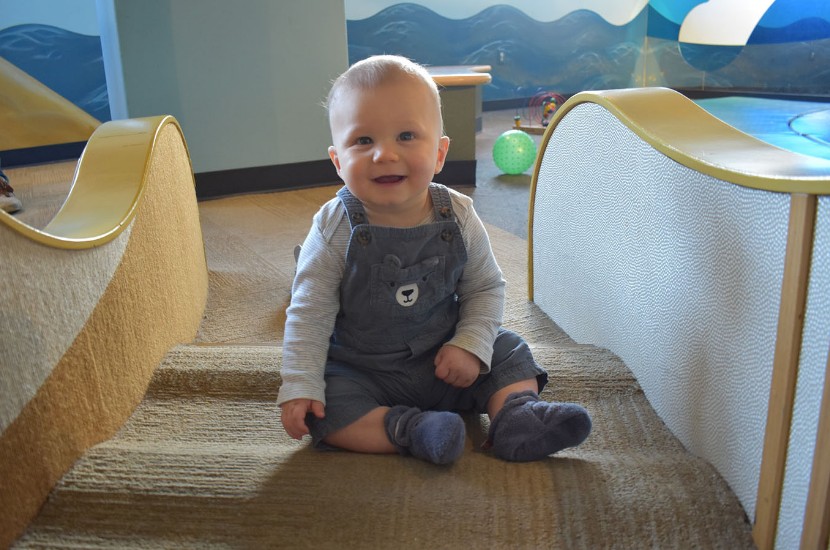 A baby smiling at the camera while sitting on a soft floor in Port Discovery's Tot Trails play area