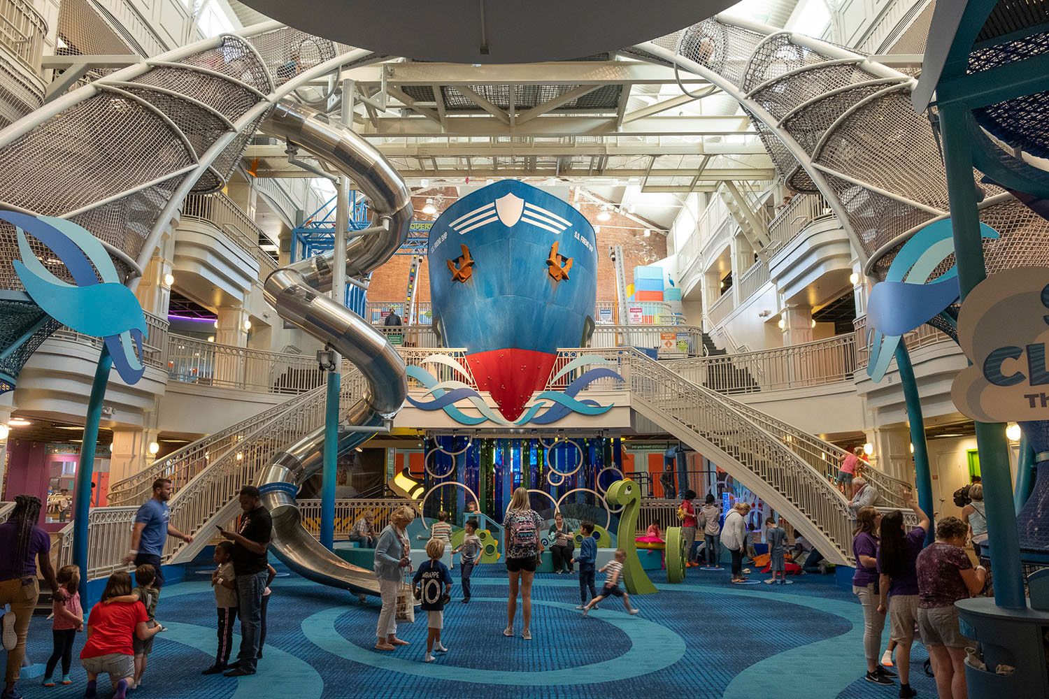 Families exploring Port Discovery's three floor Museum, including a multi-story climbing exhibit, slide and giant ship.