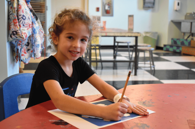 Girl smiles while drawing in the BGE Studio Workshop at Port Discovery Children's Museum