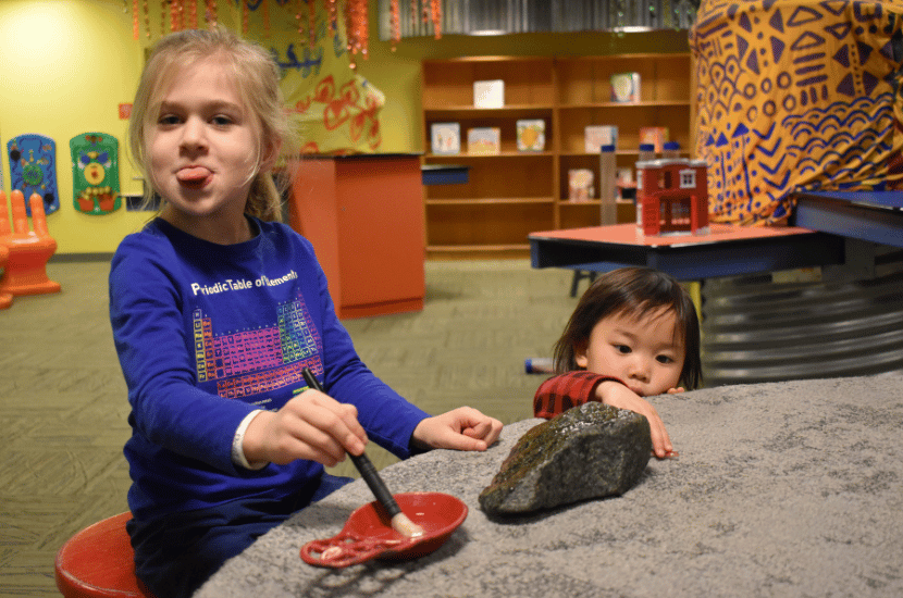 Girls play in the Oasis Exhibit at Port Discovery Children's Museum; one girl sticks her tongue out