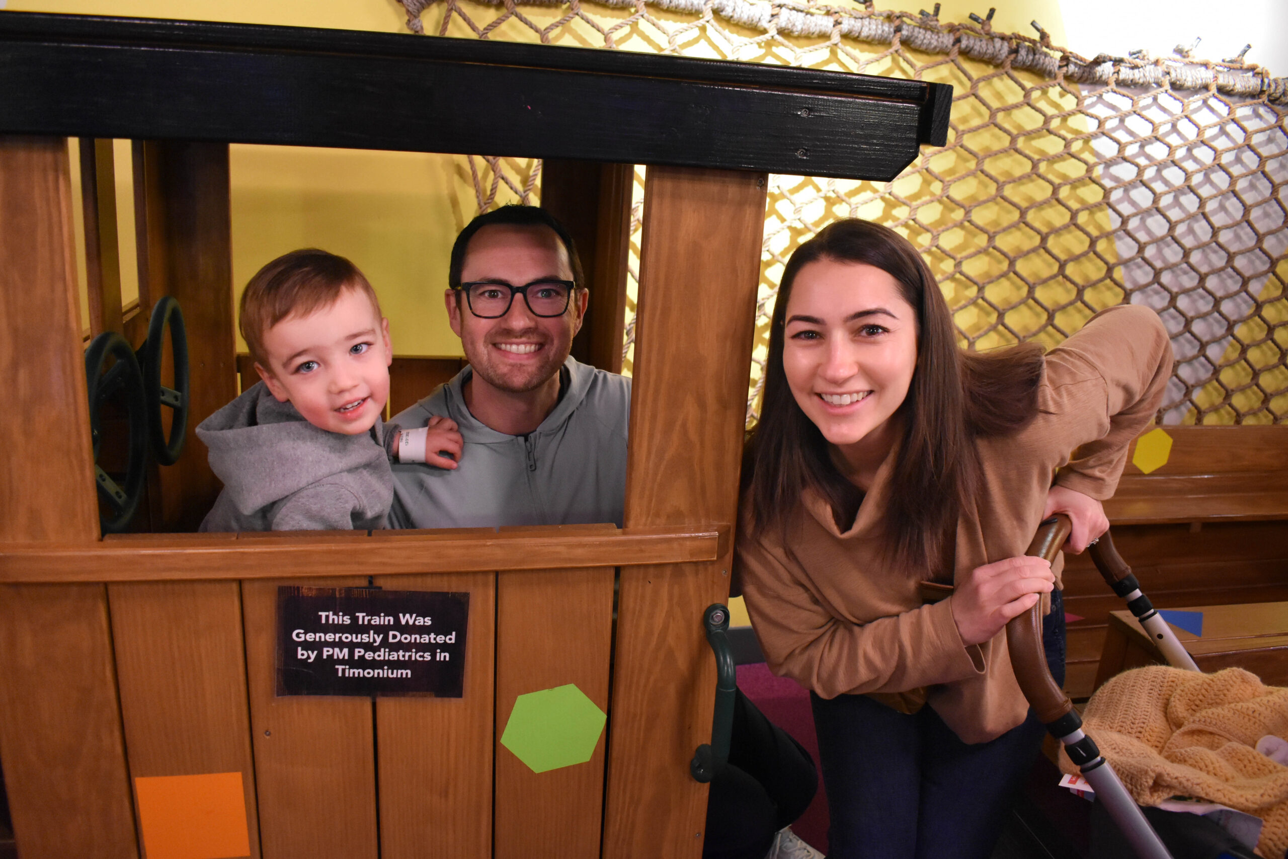 two adults are sitting with their small child in the museum train set