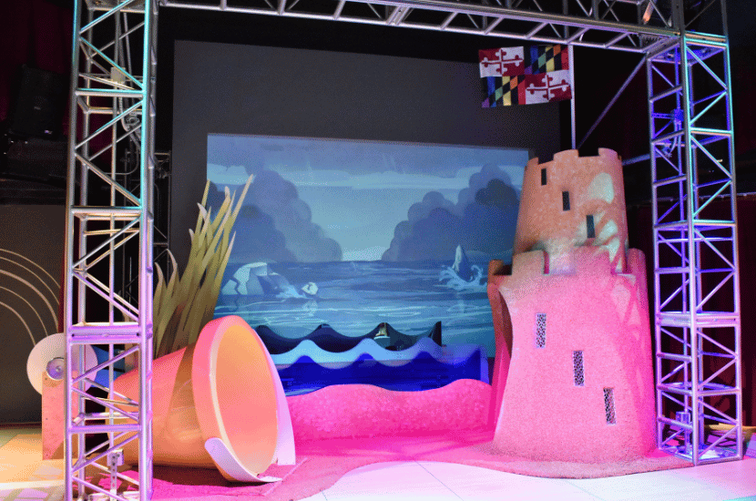 The stage at The Playhouse at Port Discovery which currently has an ocean background, a life size sand castle made out of cork and a life size sand bucket that kids can crawl through