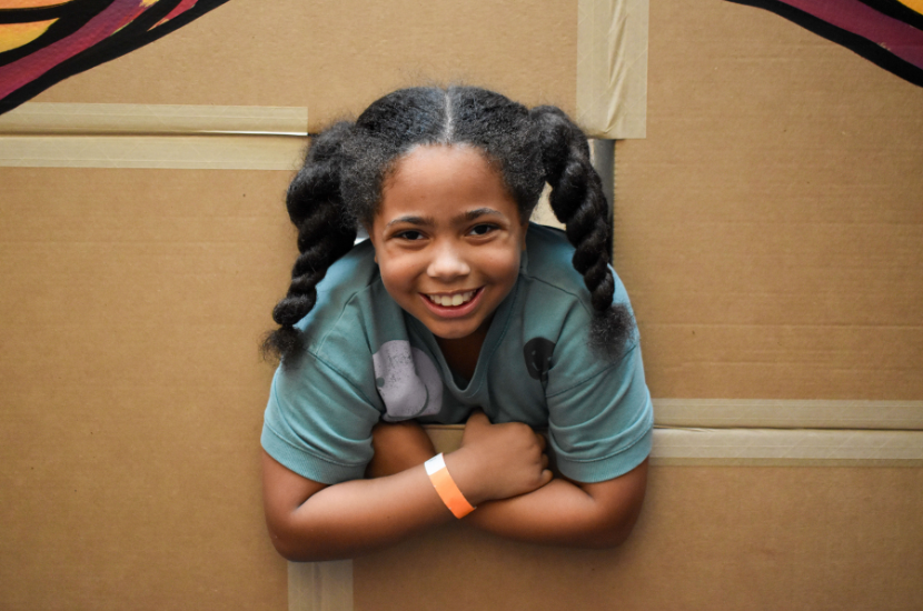 Child smiles, looking through a window in a box maze at Port Discovery Children's Museum